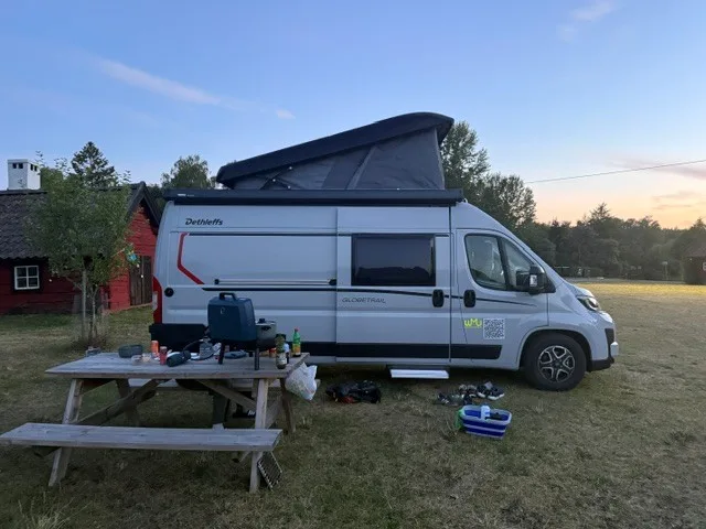 Dethleffs Globetrail mit Aufstelldach in der Abenddämmerung neben Picknicktisch und rotem Holzhaus