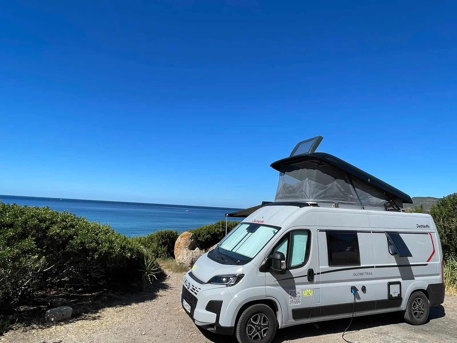 Dethleffs Globetrail mit aufgestelltem Dach an einer Küste, dahinter tiefblaues Meer